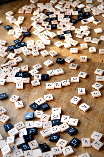 Conshohocken PA, USA - April 12, 2014: Scrabble letter tiles scattered in random order on a wooden table. Scrabble is a crossword strategy game distributed by Hasbro.