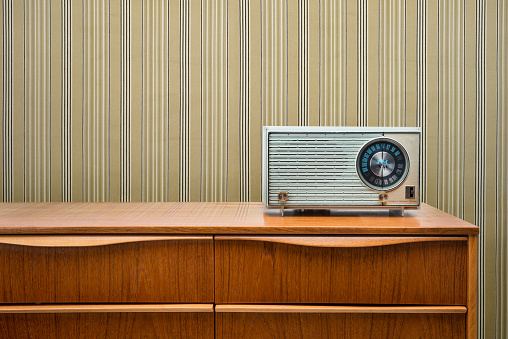 Blue vintage radio from the 1950's sitting on a mid-century modern dresser with striped wallpaper.