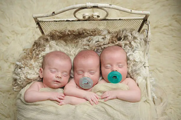 Three identical triplet brothers sleeping in a miniature bed.