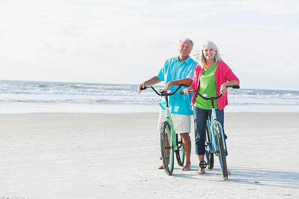 mature couple équitation vélos sur la plage - senior couple cycling beach bicycle photos et images de collection