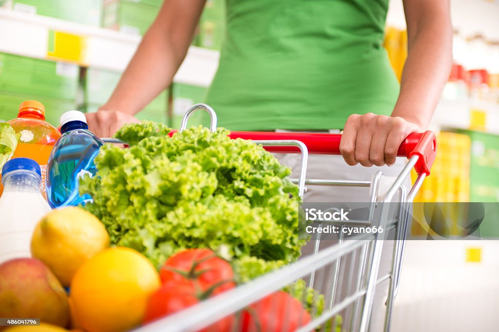 Full shopping cart Woman in green t-shirt pushing a shopping cart at store with shelves on background. 2015 Stock Photo