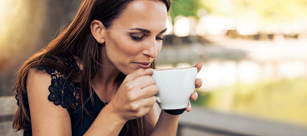 Close up portrait of young woman with an aromatic coffee in hands. Female drinking coffee at cafe.