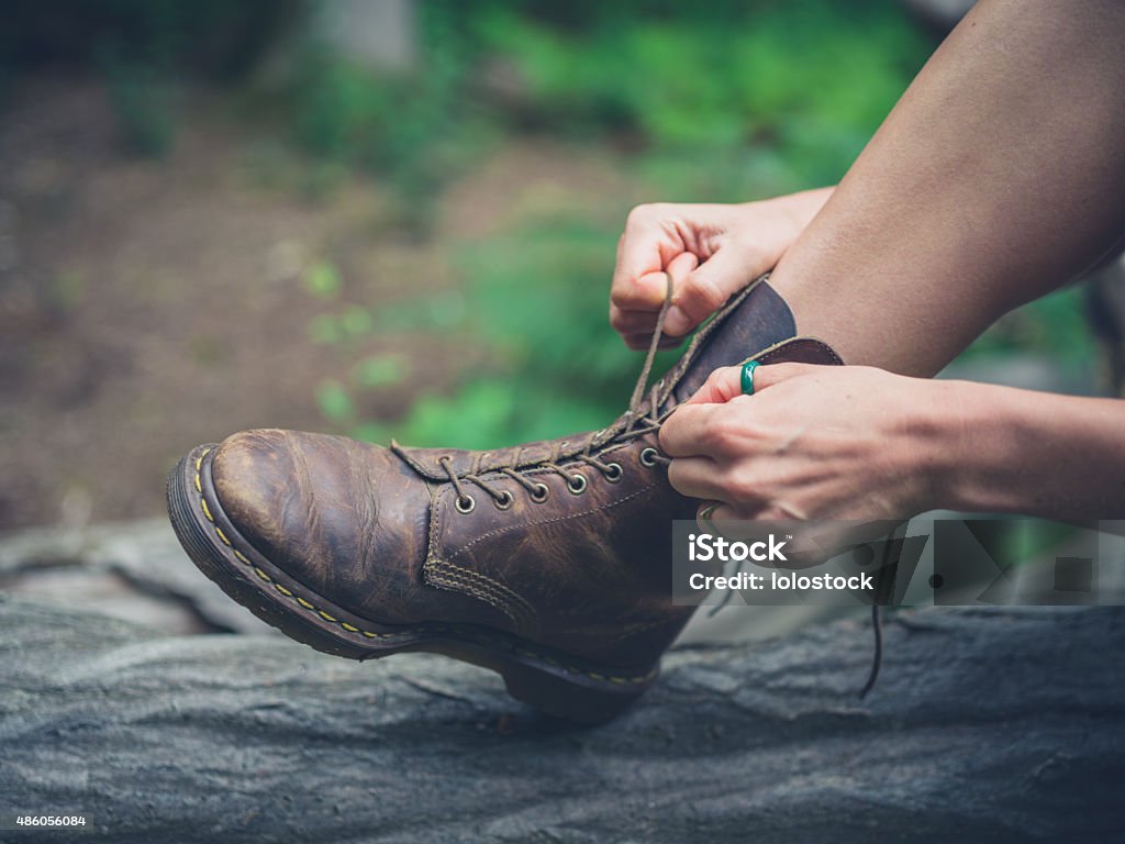 Young woman tying her boots in forest A young woman is sitting on a log in the forest and is tying her boots 2015 Stock Photo