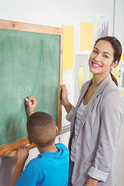 istock Pretty teacher helping pupil at chalkboard 486063406