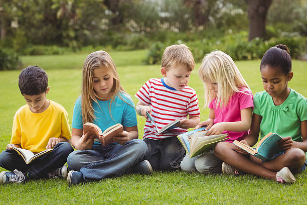 istock Classmates sitting in grass and reading books 486066612