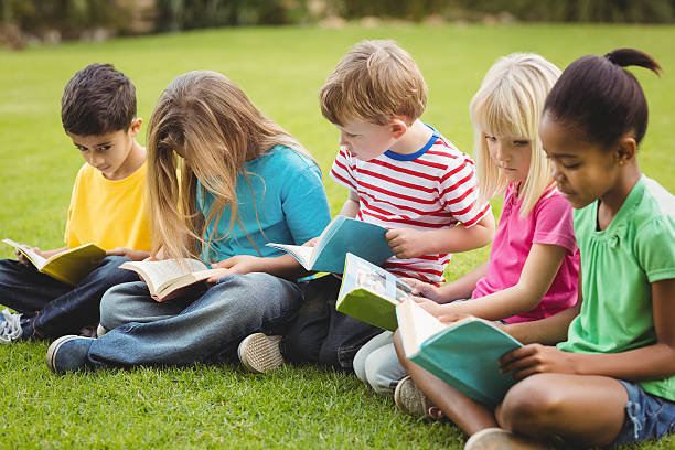 istock Classmates sitting in grass and reading books 486066614