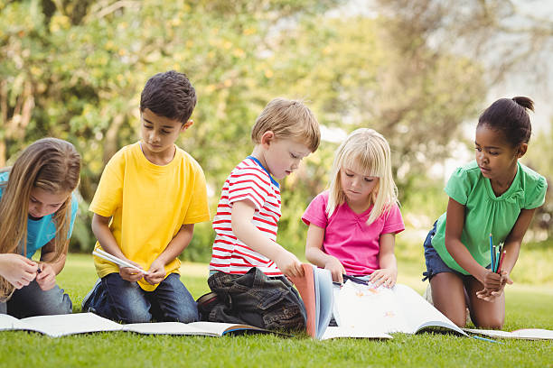 istock Classmates sitting in grass and reading books 486066618