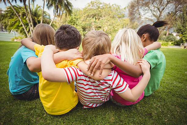 istock Happy classmates sitting in grass and having arms around 486067412