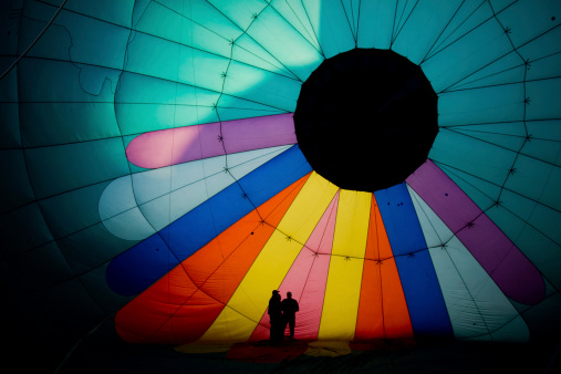 Three people standing inside of a colorful balloon that look like sun rays pointing down at them