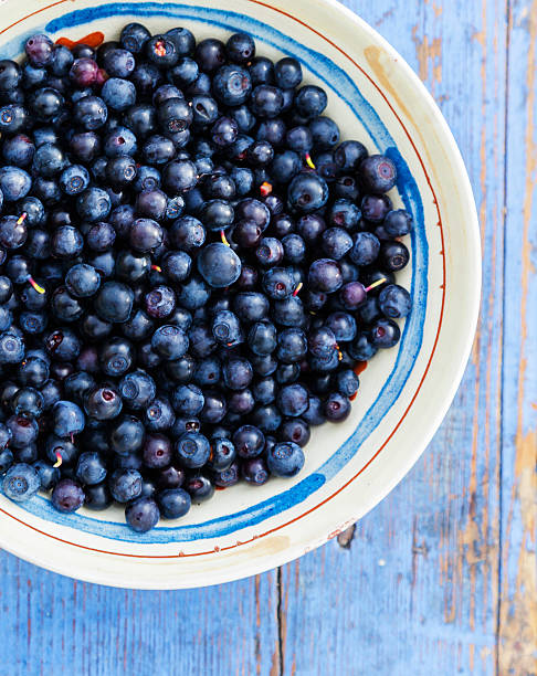 Freshly picked tasty sun-ripened blueberries in ceramic bowl on a blue stool outside.