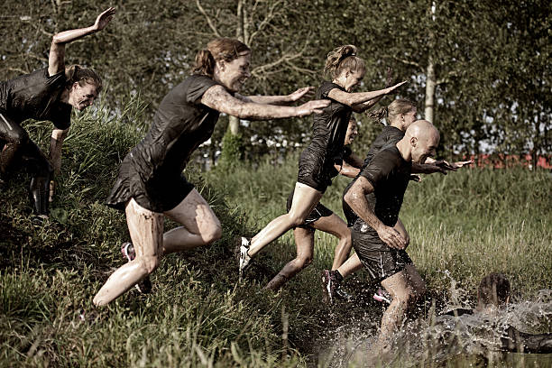 group of friends jumping into water during mud run