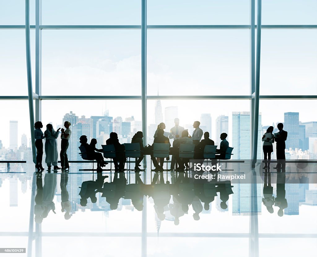 Silhouettes Of Business People Around The Conference Table With Silhouettes of business people around the conference table with a view of urban scene. Business Meeting Stock Photo