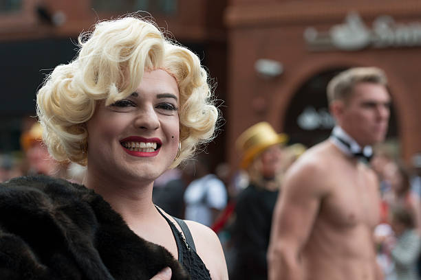 Manchester, UK - August 29, 2015: Drag Marilyn Monroe smiling while walking in the 2015 Manchester Pride Parade. Spectators line the street. out of focus topless man. Deansgate location.