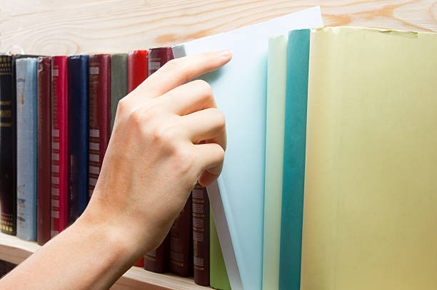istock Women Hand selecting book from a bookshelf in library. 486106356