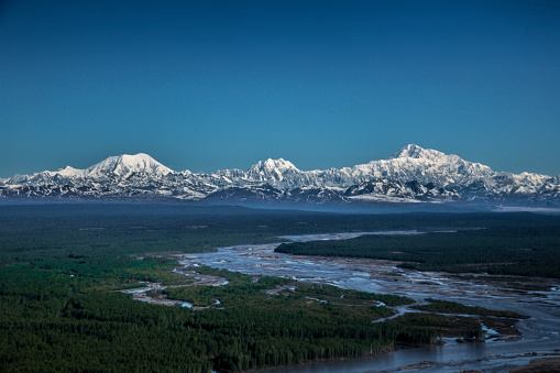 An aerial view of the tall snowy mountains of the Alaska Range, considered one of the great ranges, over the Susitna River.