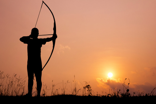 Silhouette archery shoots a bow at a target in sunset sky and cloud.