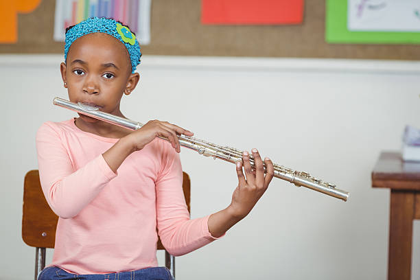 Cute pupil playing flute in a classroom