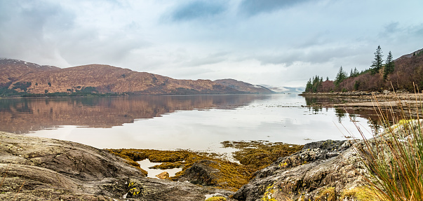Panoramic winter scene in the Scottish Highlands with snowy mountains and colorful hills mirroring in the calm lake. Loch Linnhe, Scotland, Great Britain.