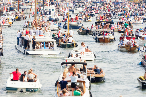 Color image of a very large group of boats and people sailing on Ij river in Amsterdam, the Netherlands. Selective focus on the background.