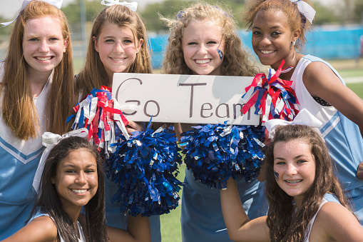 Multi-ethnic group of high school cheerleaders wearing blue uniforms with pom-poms and a \