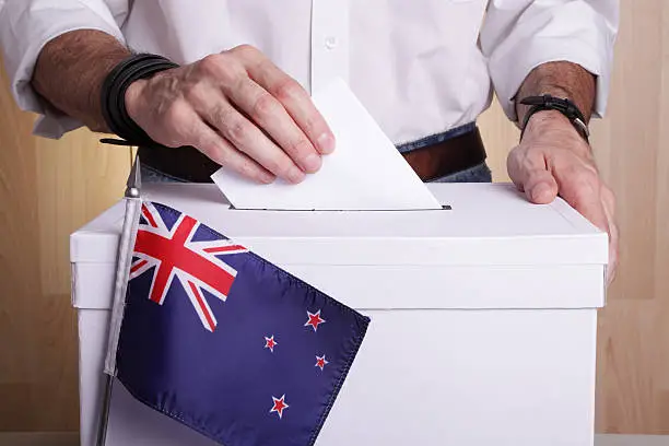 A man casting his vote. The New Zealand flag is in front of the ballot box
