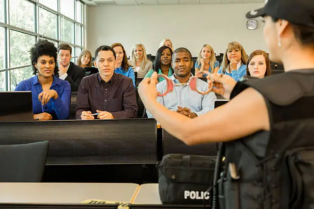 Photo of Law:  Policewoman speaks to police cadets in classroom. Handcuffs.