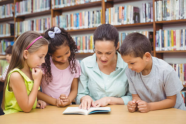 istock Pupils and teacher reading book in library 486149160