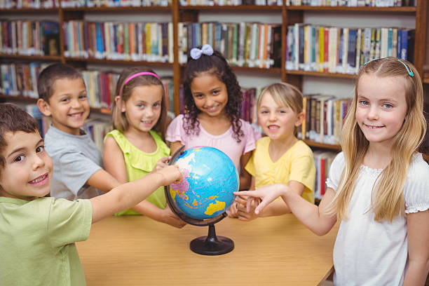 istock Pupils smiling at camera in library pointing to globe 486150642