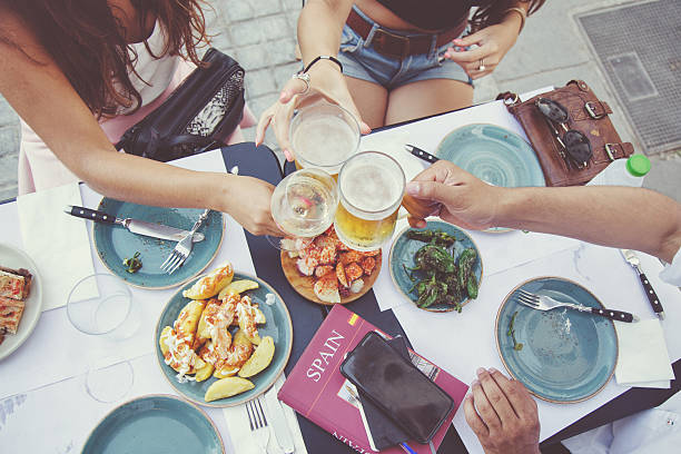 Tapas and beer toast Tourists in Barcelona eating tapas in a typical restaurant in the Barri Gotic. On the table a travel guide of Spain and a smartphone. patatas bravas stock pictures, royalty-free photos & images