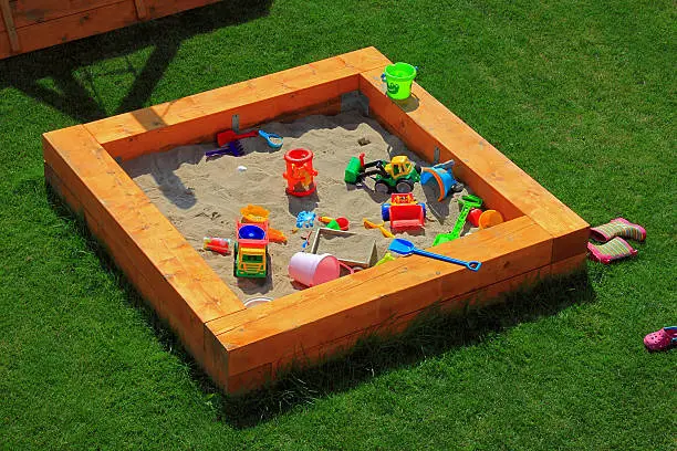 A nice sandbox playground filled with lots of toys. Surrounded by green grass, seen from top.