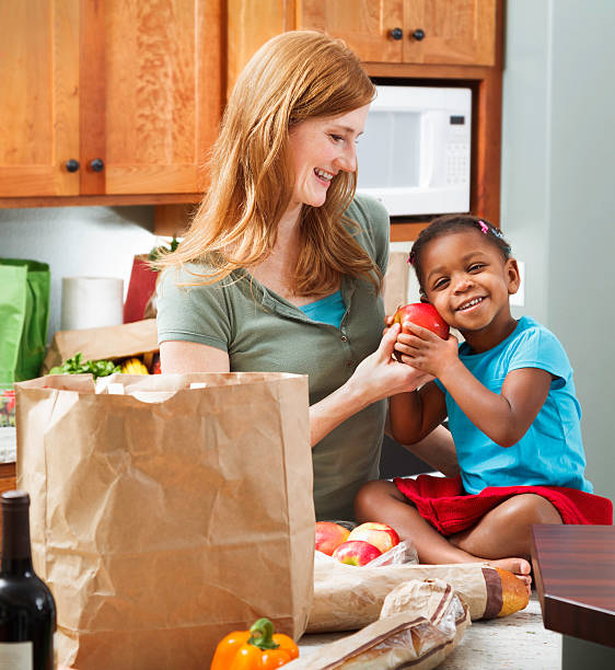 istock mother smiling at adopted daughter in kitchen with groceries 486164529