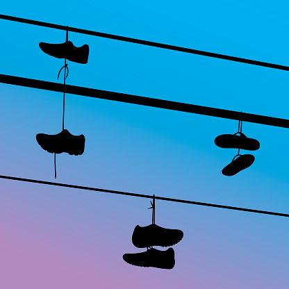 Vector silhouettes of various shoes hanging on telephone wires against a blue/purple evening sky.