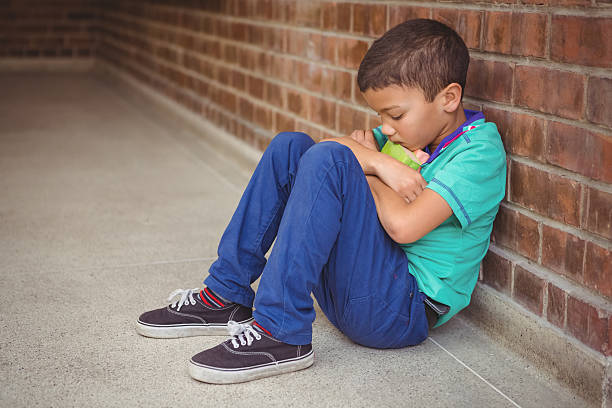 Upset lonely child sitting by himself Upset lonely child sitting by himself on the elementary school grounds school exclusion stock pictures, royalty-free photos & images