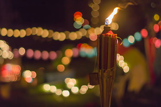 Tiki Torch at Night with lots of Bokeh A lit tiki torch at night with lots of multi-colored bokeh in the background tiki torch stock pictures, royalty-free photos & images