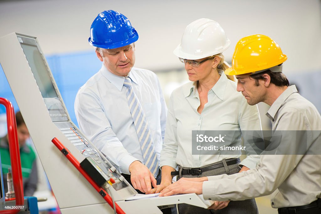 Engineers Programming A CNC Machine Team of engineers programming a CNC machine at the manufacturing plant. Adult Stock Photo