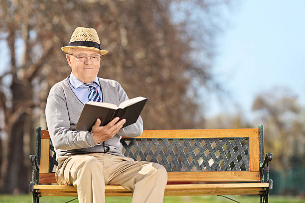 istock Senior sitting on bench and reading book in park 486202789