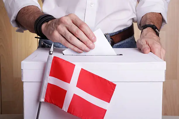 A man inserting a ballot to a ballot box.  Danish flag in front of it