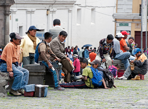 Quito, Ecuador - November 15, 2014: Poor locals chatter whilst they gather on stone benches in the Plaza de San Francisco, whilst waiting for state and charitable handouts in the early morning in old Quito, Ecuador