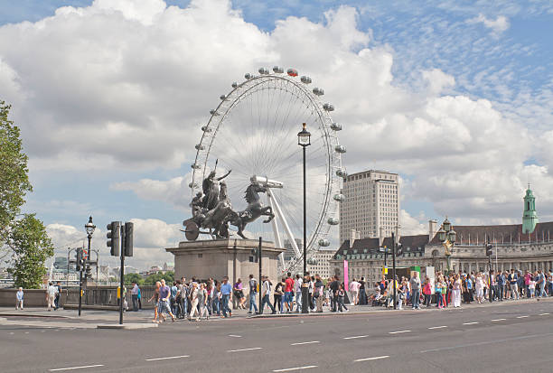London/England: May 6th,2014: Traditional British people and tourists in Westminster crossing the street in a typical busy day in London. Image shows the wheel (London Eye) on the background.