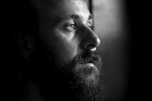 Close-up photo of a serious man with a beard in profile. Black and white image with shallow depth of field