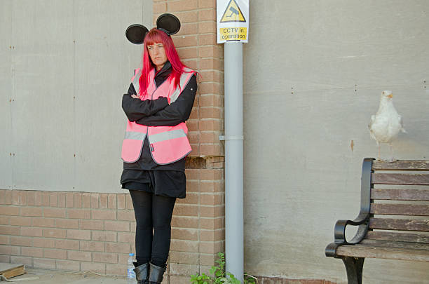 Dismaland happy helper Weston-Super-Mare, UK - August 26, 2015: An happy helper at the Banksy-inspired Dismaland parody theme park.  Assistants wearing round ears fashioned from old can tin lids look on grim faced throughout the display at a disused swimming pool at the Somerset resort. banksy stock pictures, royalty-free photos & images