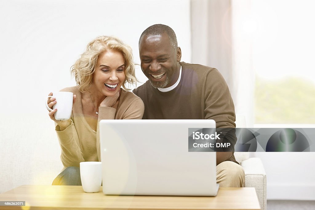 Cheerful mature couple using wireless technology at home Cheerful mature couple using laptop computer while sitting at home Couple - Relationship Stock Photo