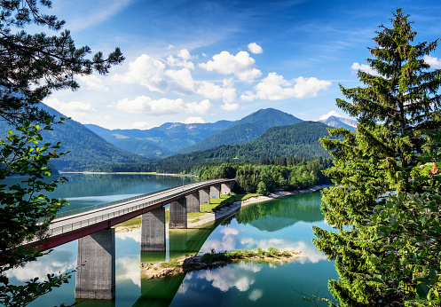 A mountain landscape with a lake and bridge in European Alps in summer, aerial view.