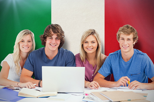 A group of students with a laptop look into the camera against italy national flag