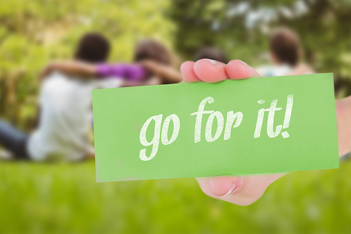 The word go for it! and hand showing card against children sitting with arms around at park