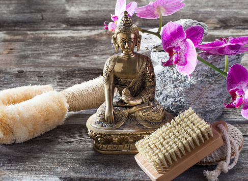 spa beauty treatment concept - symbol of washing-up and exfoliation for inner beauty with Buddha on old wood, gray texture stones and pink orchid flower background for authentic retreat decor