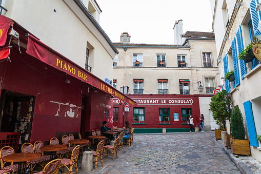 Paris, France - September 25, 2013: Montmartre street scene in the city's 18th arrondissement, where two persons can be seen walking on the cobblestone streets while a man and a woman are sitting outside a restaurant.  This historic district used to be a village but was annexed to Paris in 1860. 