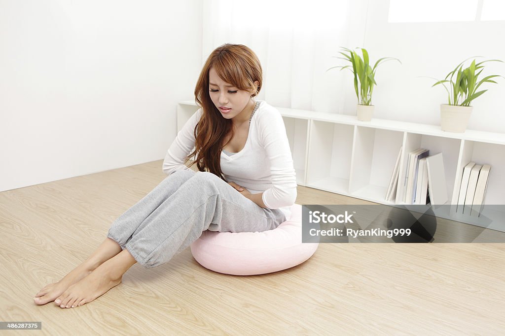 woman with stomach ache Portrait of woman with stomach ache sitting on floor at home, asian model Stomachache Stock Photo