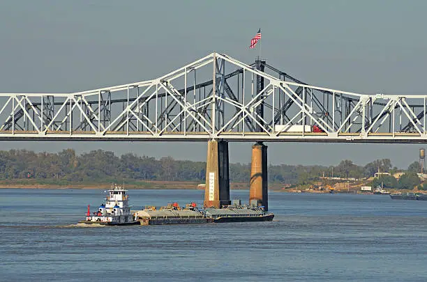 Tug boat and barges of petrolium oil passes under the Vicksburg Bridge along the Mississippi River