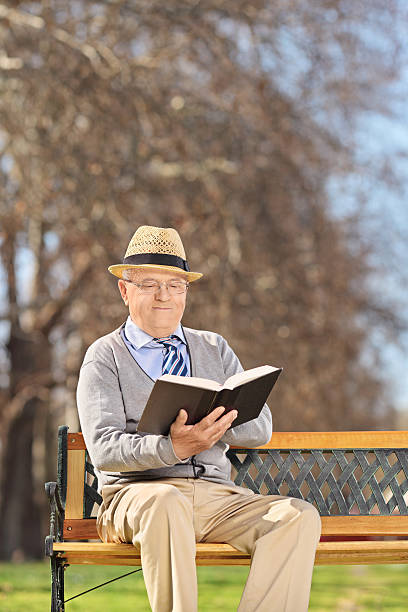 istock Senior sitting on bench and reading book in park 486310549